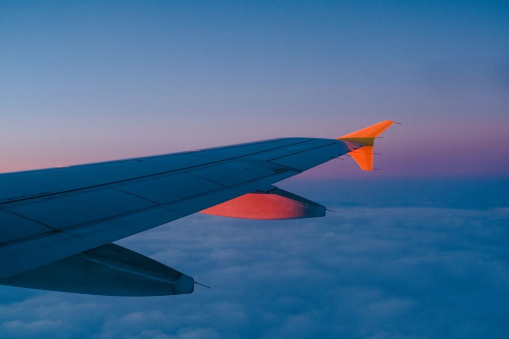 A view of an airplane wing soaring above clouds during sunset, showcasing a serene sky.