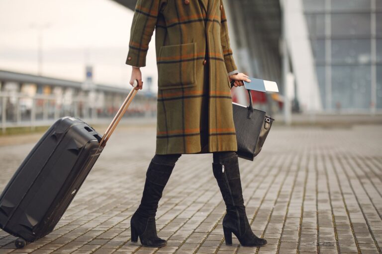 Woman wearing a coat rolling a black suitcase and holding a passport and boarding pass
