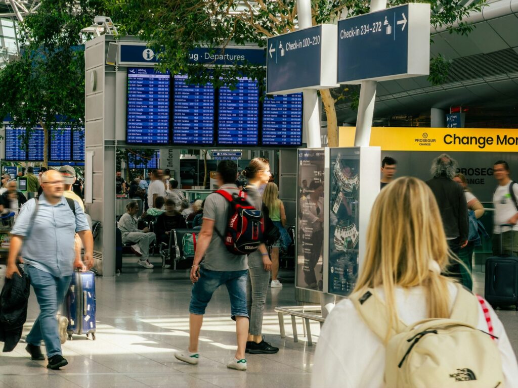 People walking through a busy airport terminal with flight departure boards, where Global Entry families pass through