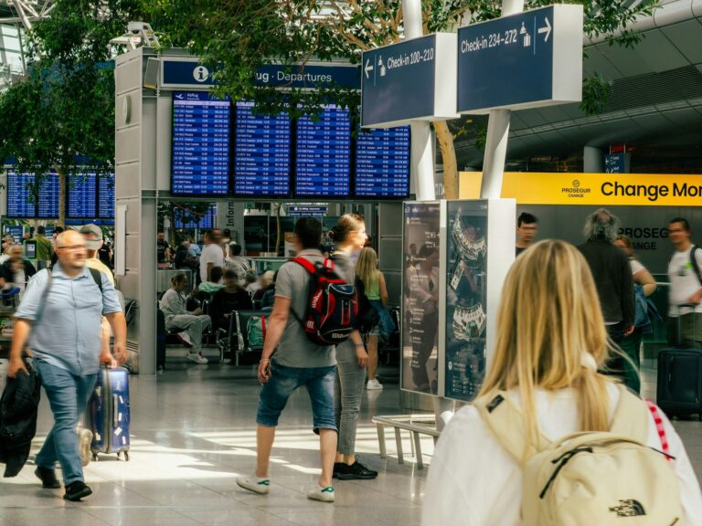 People walking through a busy airport terminal with flight departure boards, where Global Entry families pass through
