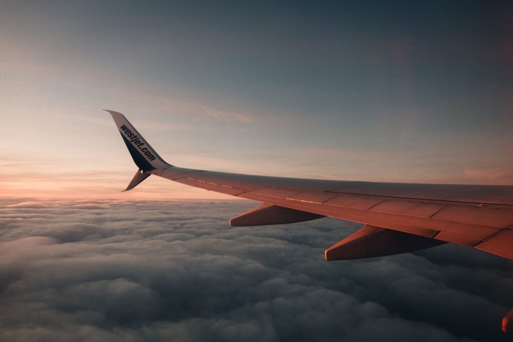 A breathtaking view of an airplane wing during a flight above clouds at sunset