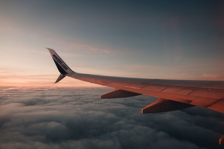 A breathtaking view of an airplane wing during a flight above clouds at sunset