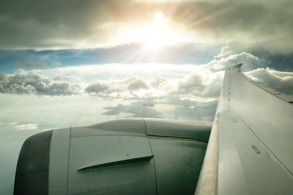 Scenic view of an airplane wing flying above fluffy clouds with the sun shining through